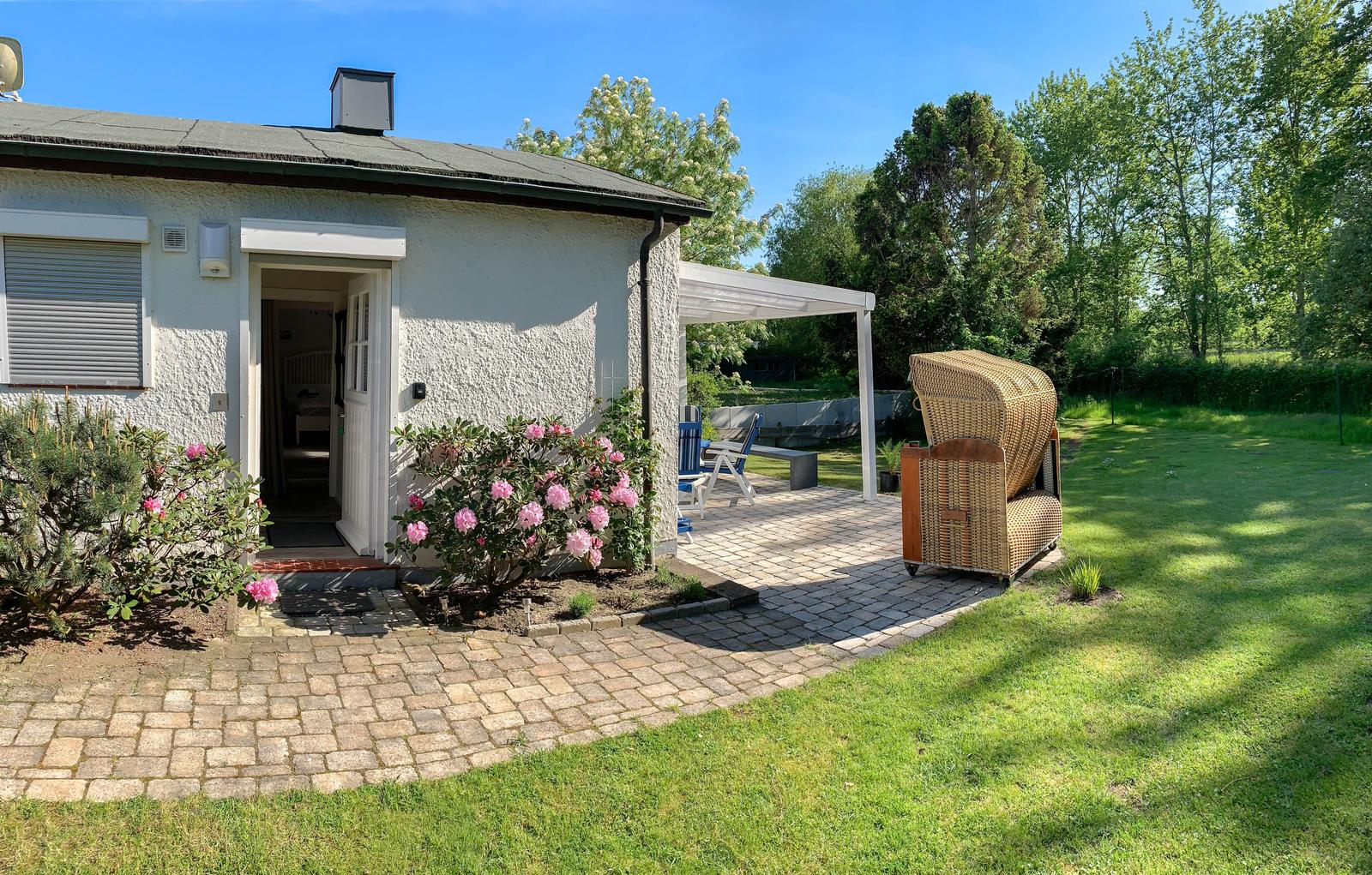Haus mit Terrasse, Garten und Blick auf Wald. Eingangsbereich mit Blumen.