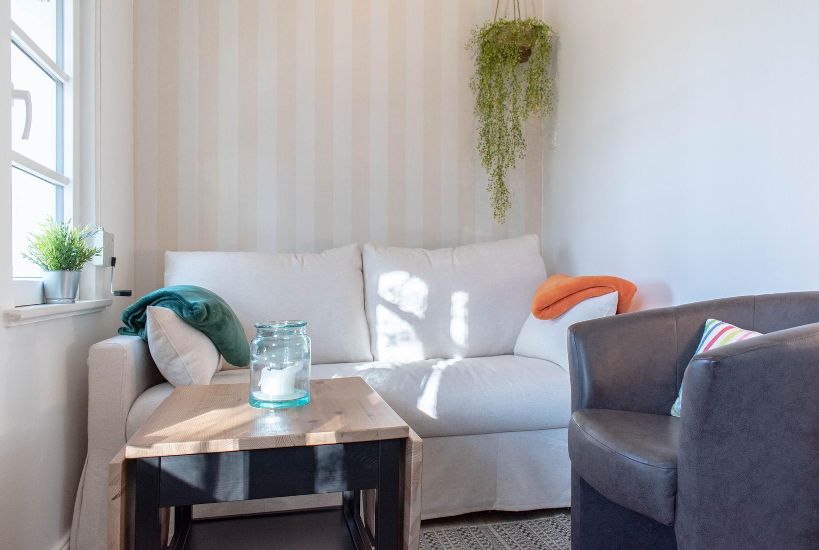 Ein Wohnzimmer mit Sofa, Sessel, Tisch und Pflanzen. Wand mit Streifenmuster.