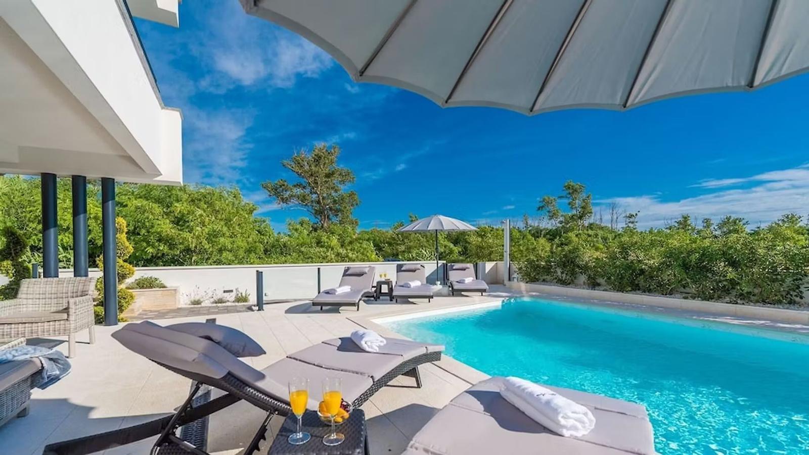 Pool area with loungers and umbrellas under blue sky.