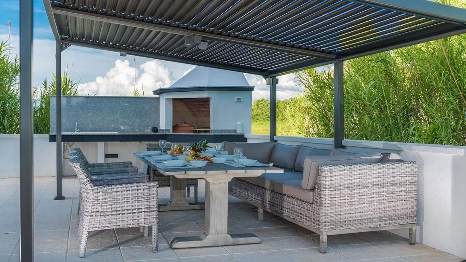 Terrace with seating group, dining table, and grill area under roof.