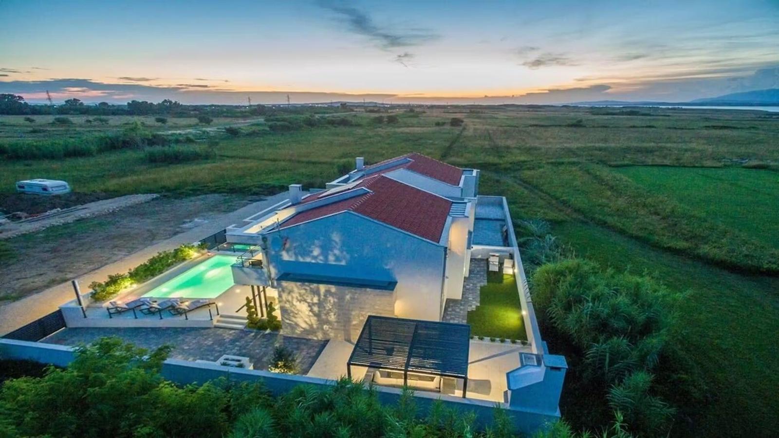 Modern villa with pool and terrace in rural setting at sunset.