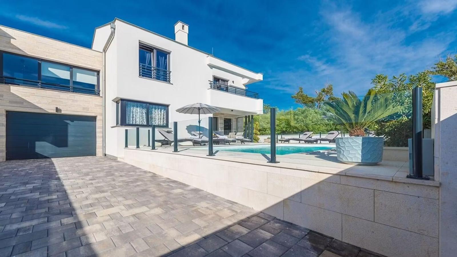 Modern villa with pool and terrace. Garage and plants are visible.