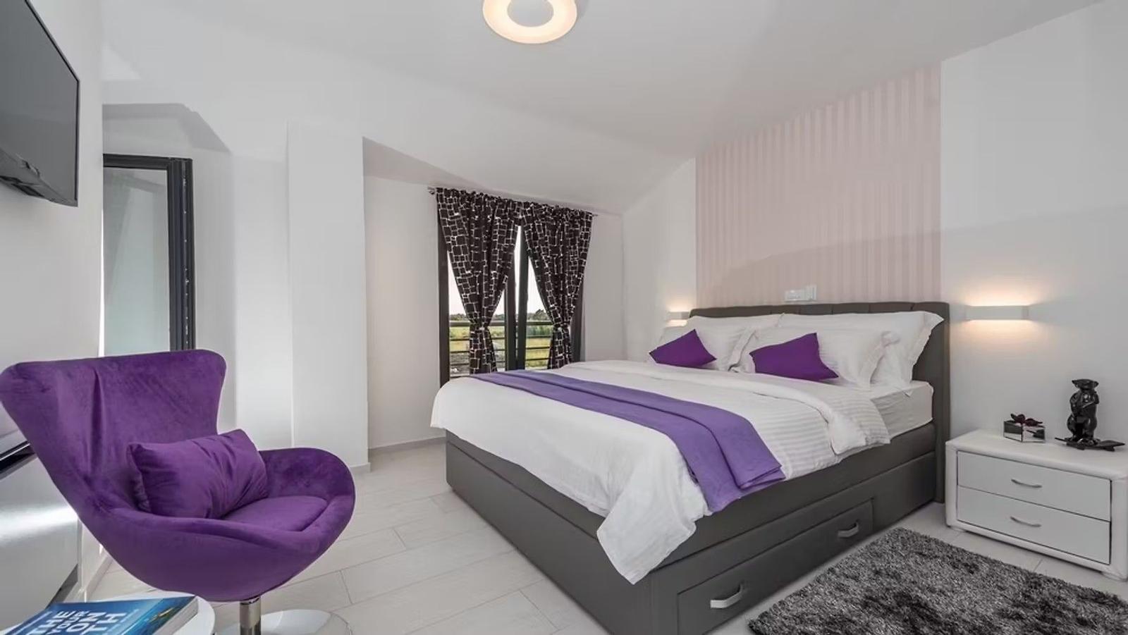 Bedroom with bed, purple chair, and window overlooking outdoors.