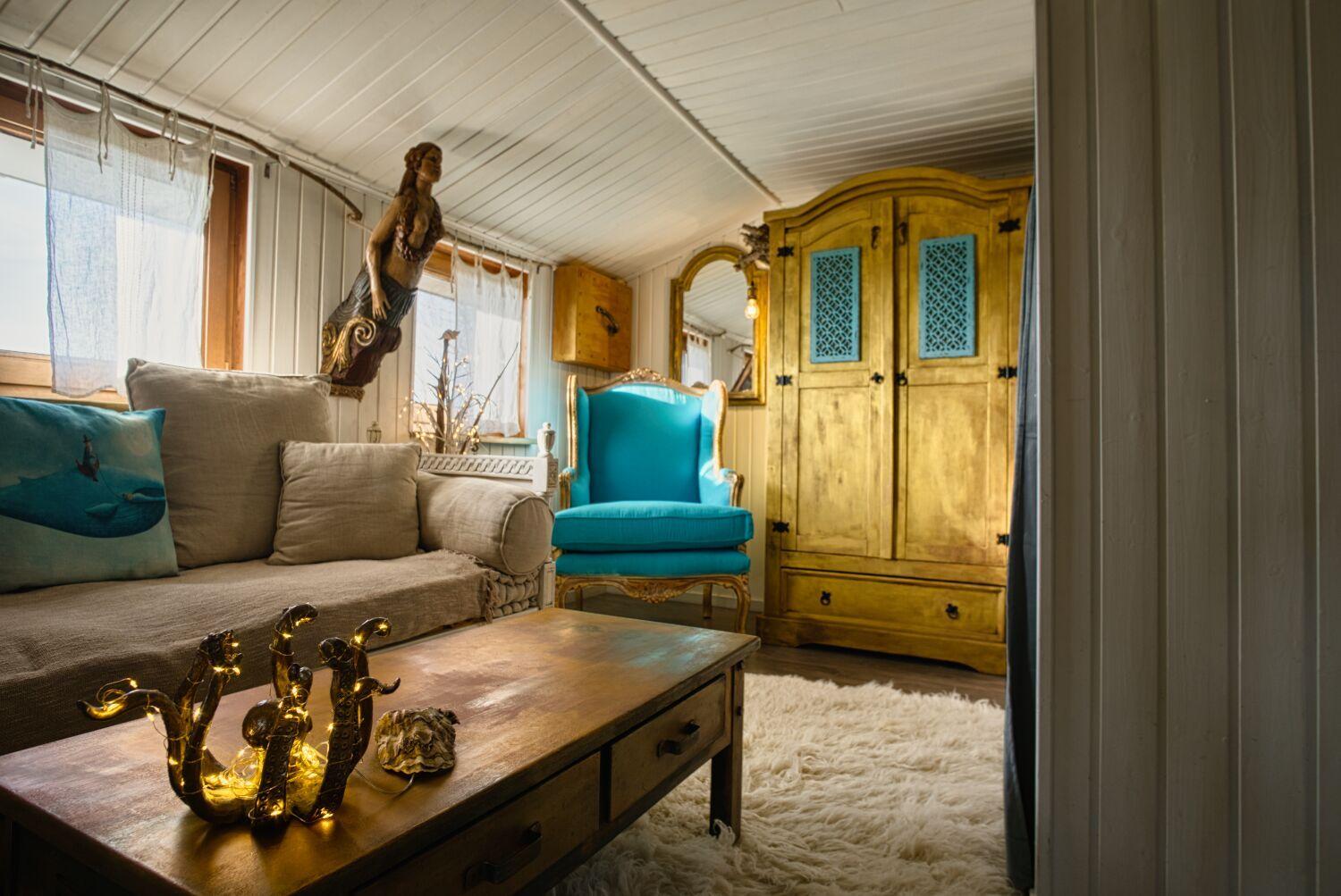 Ein Wohnzimmer mit Sofa, blauem Stuhl und Holzschrank. Auf dem Tisch stehen dekorative Objekte.