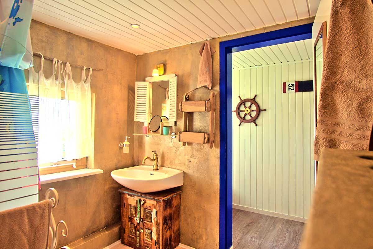 Badezimmer mit Waschbecken auf Holzschrank, Spiegel und Tür zum Duschbereich mit Ruder.