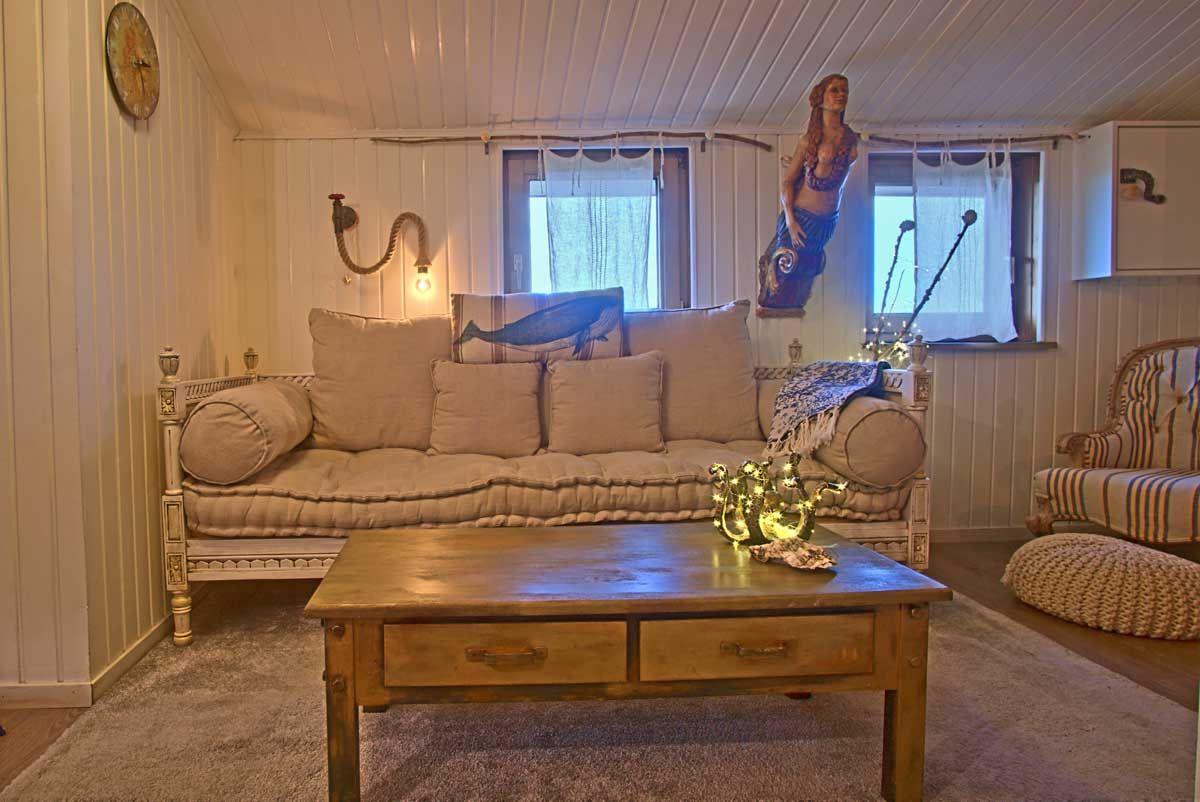 Ein Wohnzimmer mit Sofa, Couchtisch und Fenstern. An der Wand hängt eine Meerjungfrau.