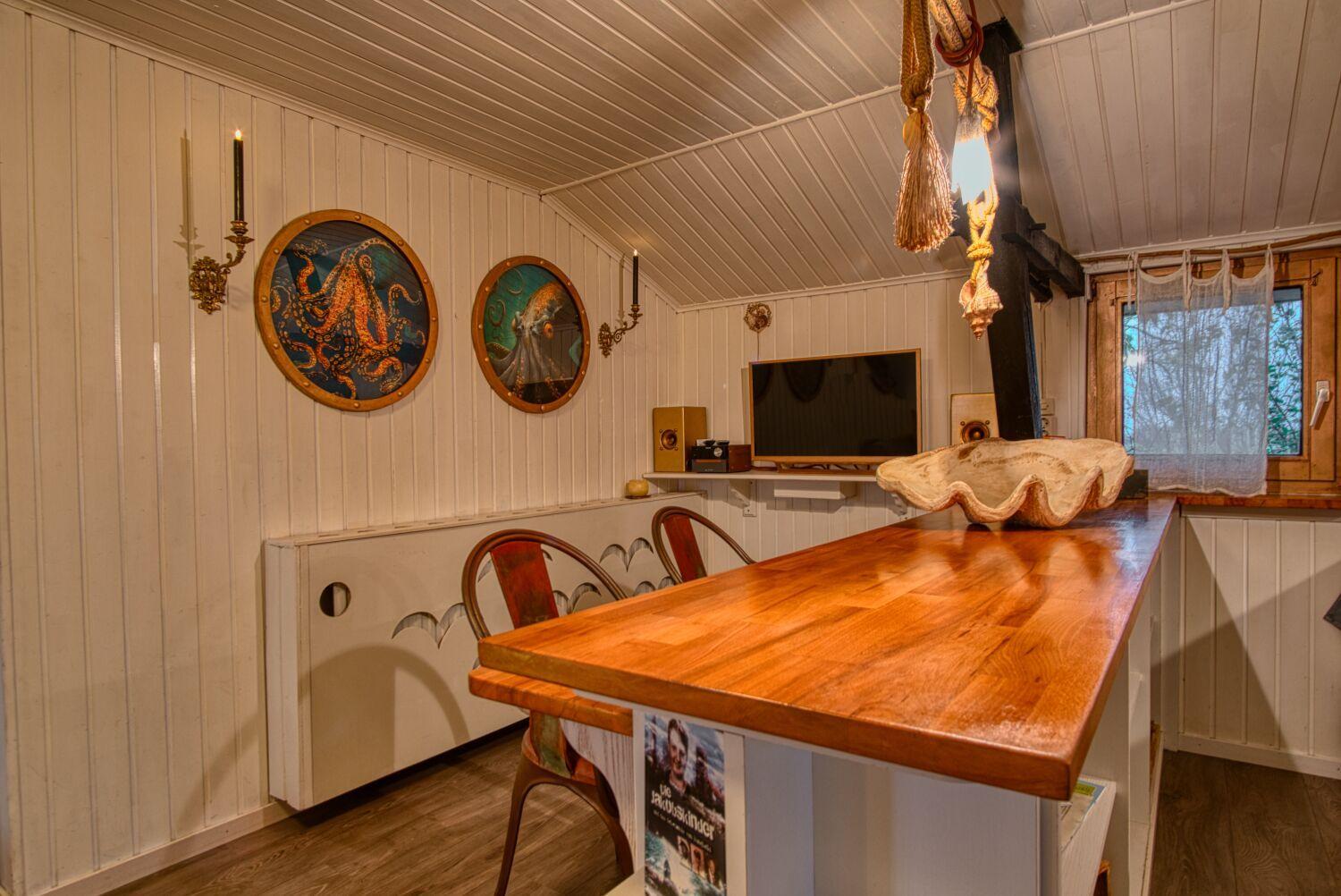 Küche mit Holztisch, Wandbildern und TV. Fenster mit Vorhang.