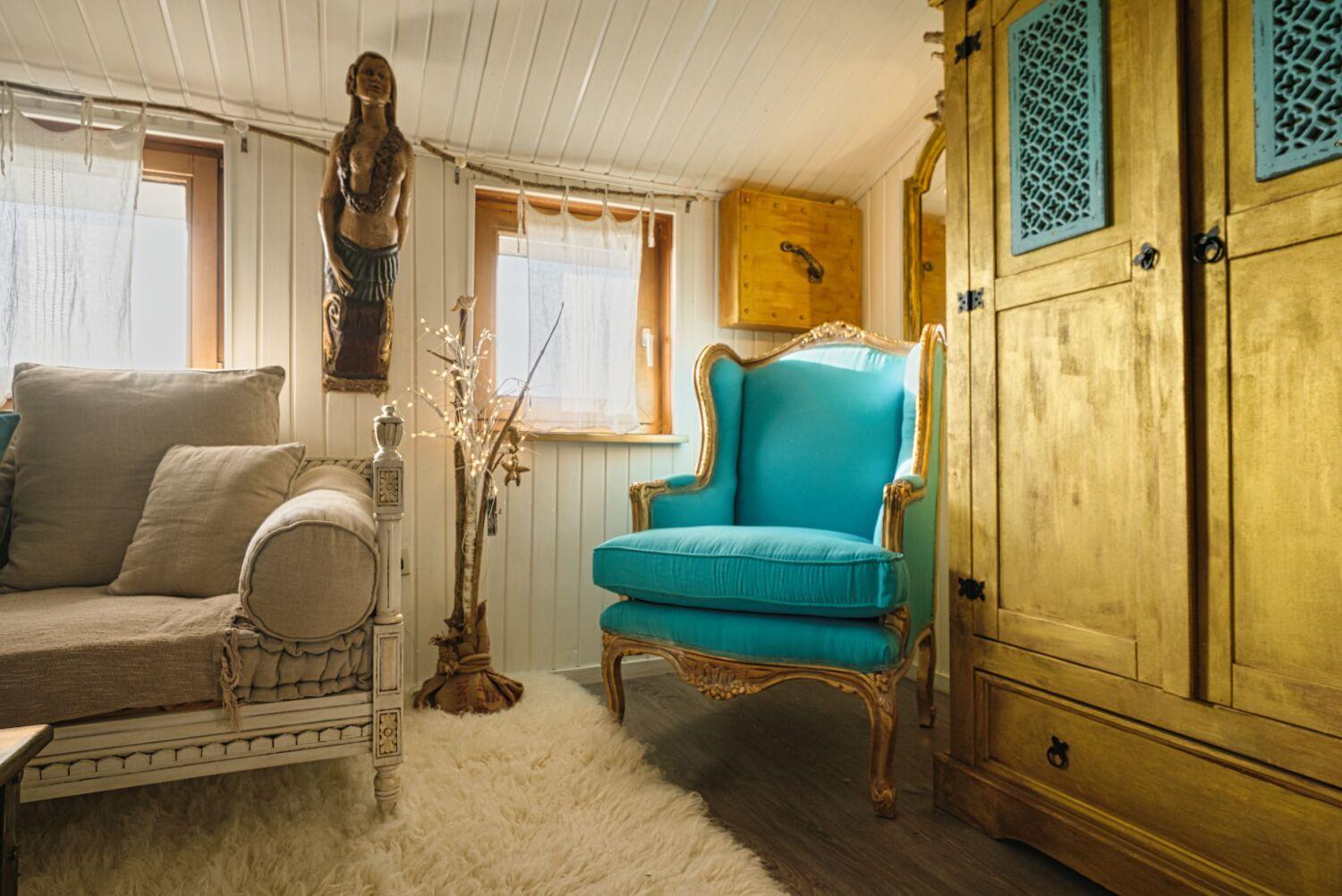 Ein Raum mit einem blauen Sessel, einem Sofa und einem großen Schrank.