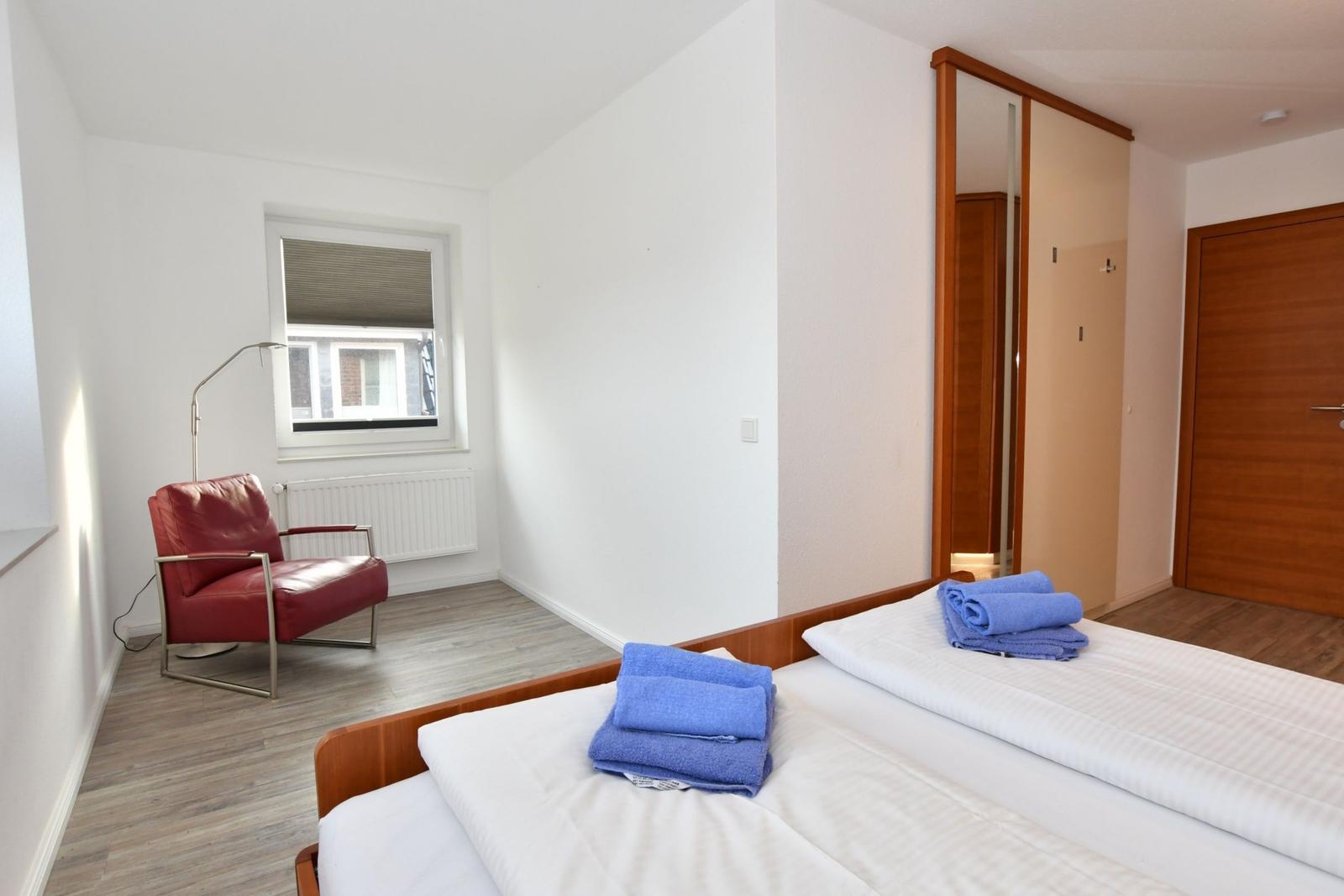 Schlafzimmer mit Bett, rotem Sessel und Kleiderschrank.