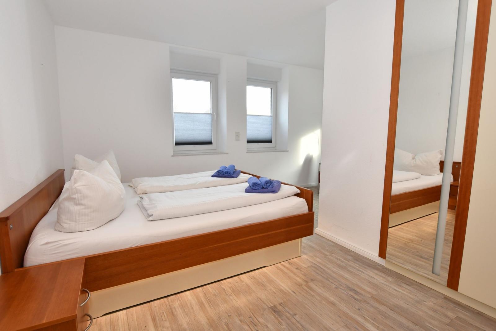 Schlafzimmer mit Doppelbett, zwei Fenstern und Spiegeltüren.