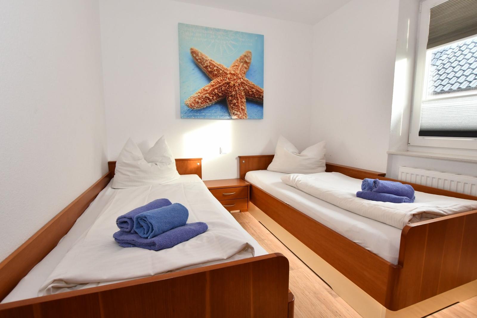 Zwei Einzelbetten mit weißen Laken und blauen Handtüchern. Wandbild mit Seestern.