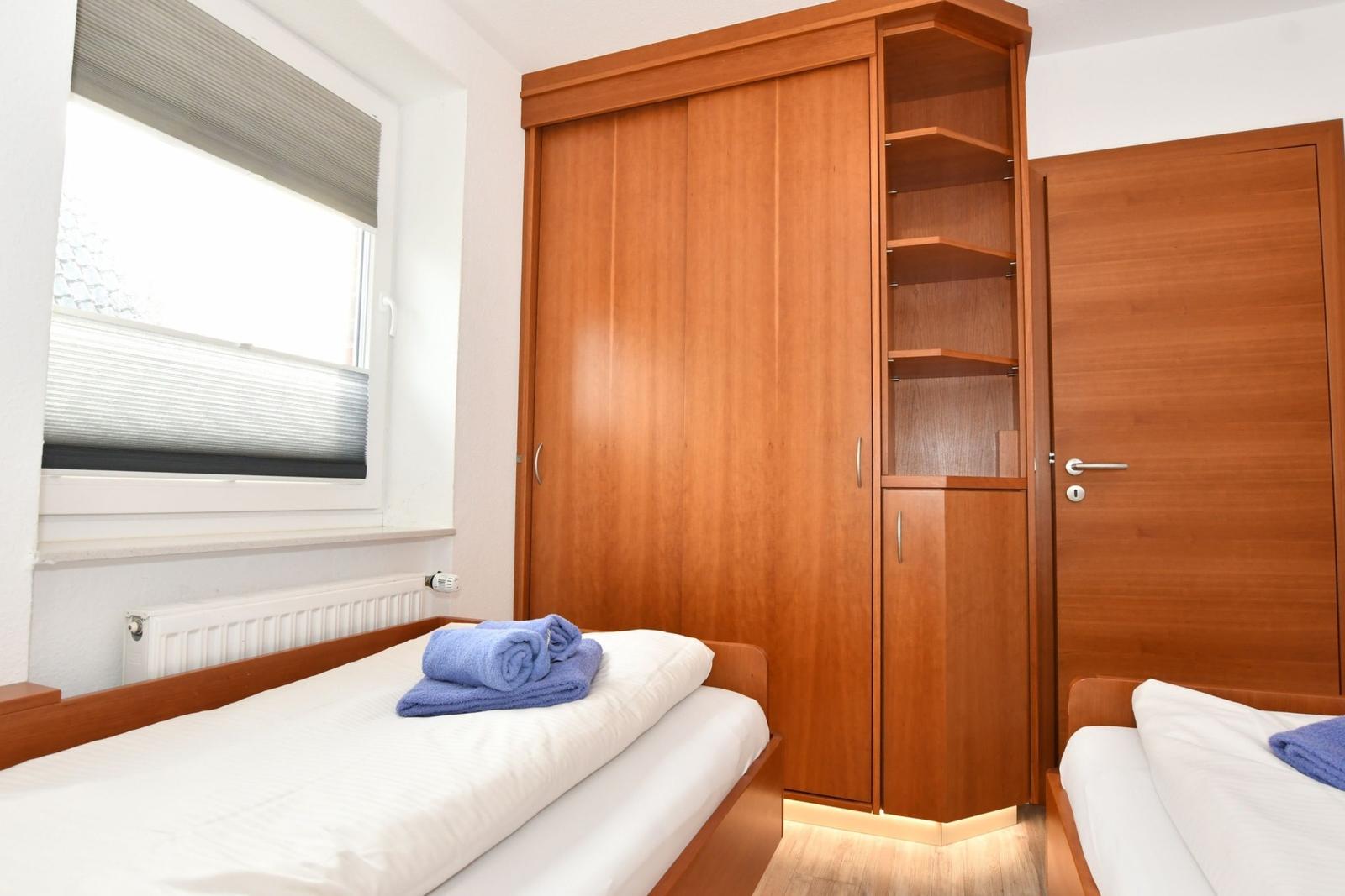 Zimmer mit zwei Betten, Holzschrank und Fenster mit Jalousie.