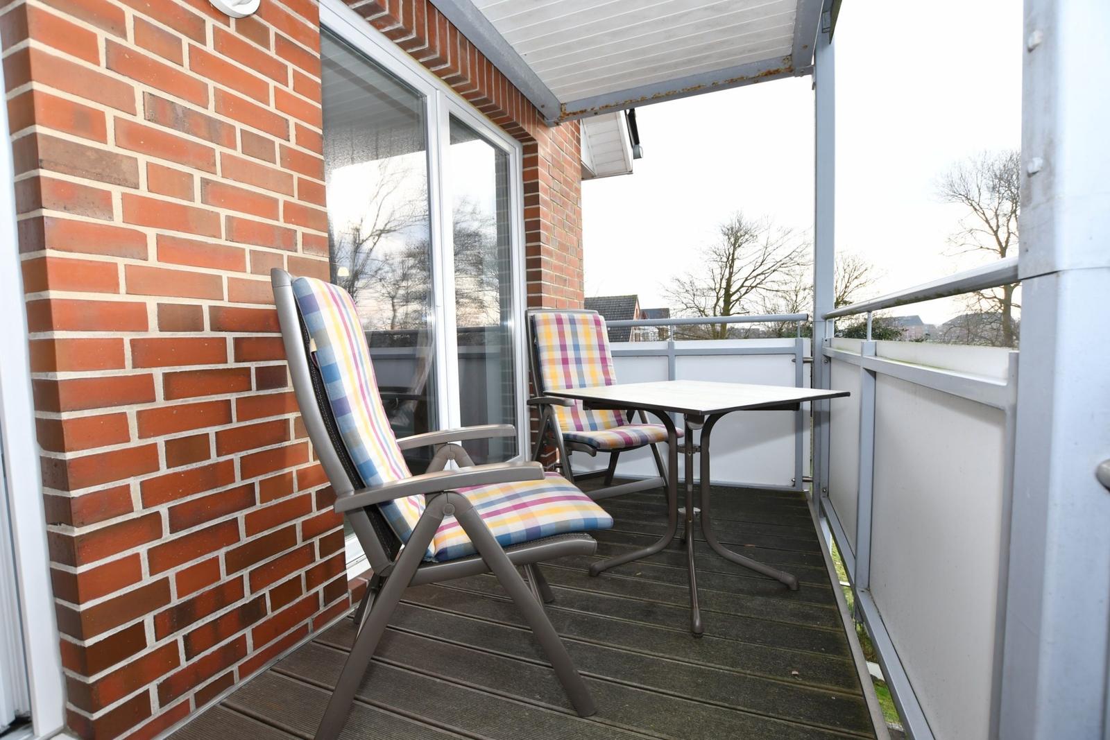 Terrasse mit Tisch und zwei Stühlen, Wand aus roten Ziegeln, Blick auf Bäume.
