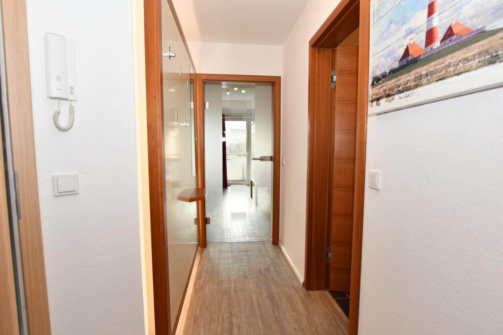 Flur mit Holzboden, Tür zu Bad und Schlafzimmer, Wandbild und Intercom.