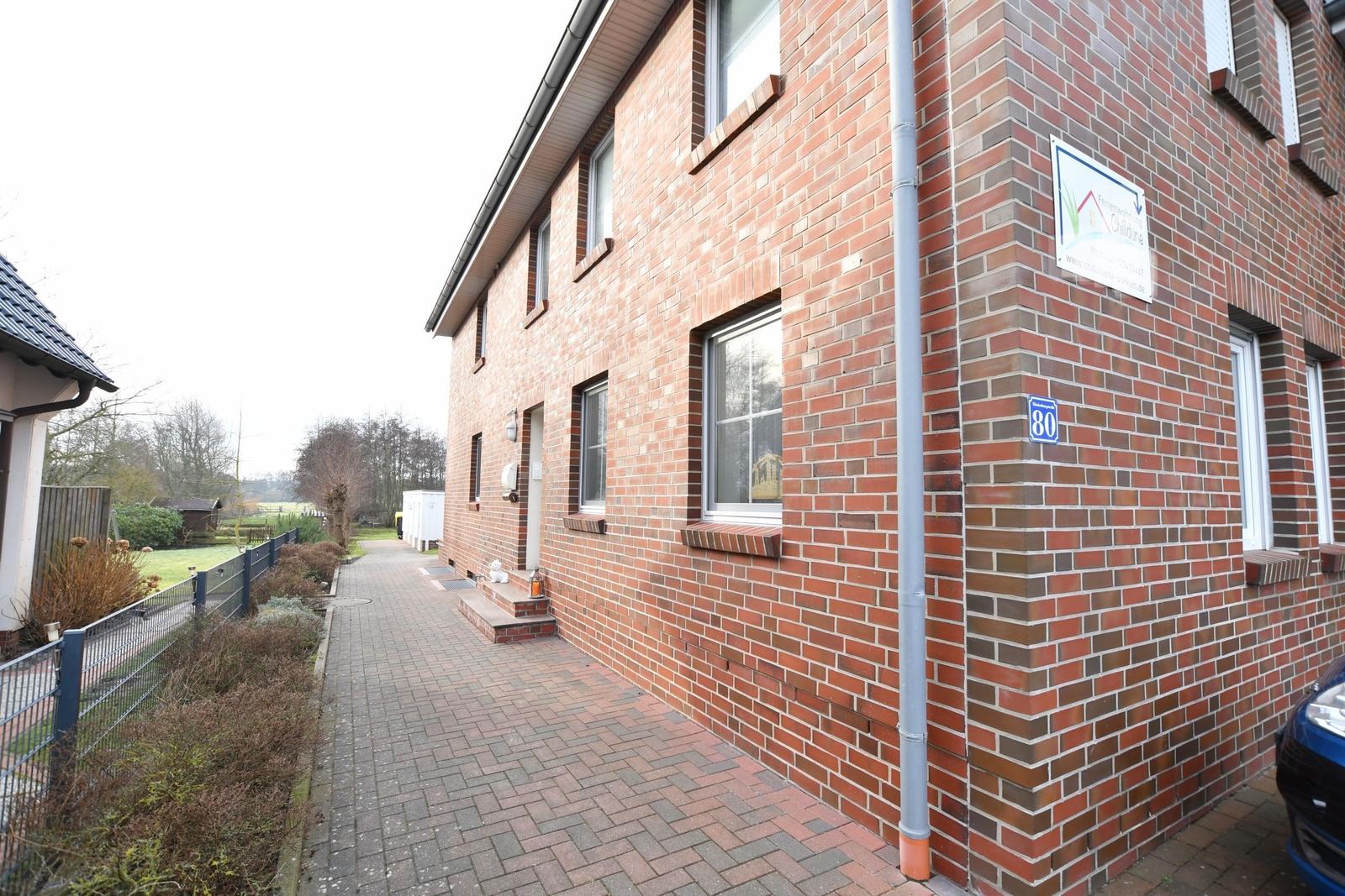 Rotes Backsteinhaus mit Fenstern und Hausnummer 80. Pflasterweg und Gartenbereich.