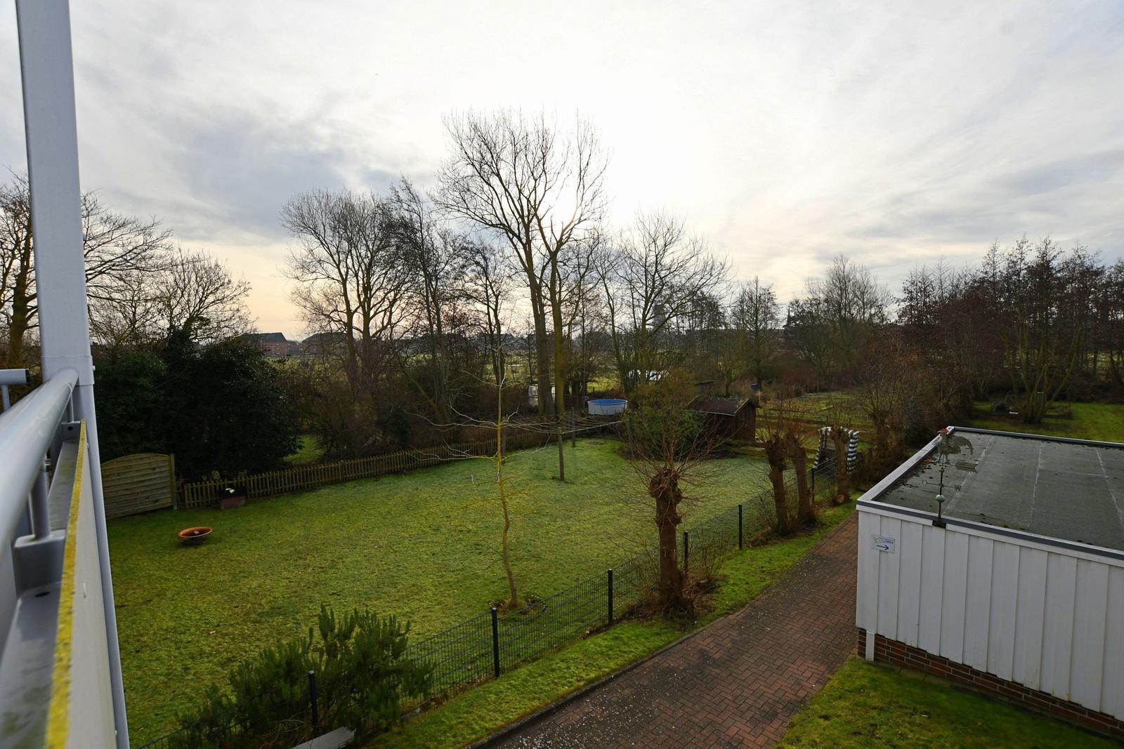 Grüner Garten mit Zaun, Bäumen und Terrasse. Blick auf einen Pool und einen Holzschuppen.