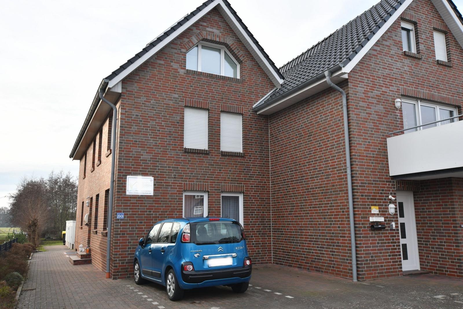 Zweistöckiges Haus mit rotem Ziegelmauerwerk und blauem Auto vor dem Eingang.