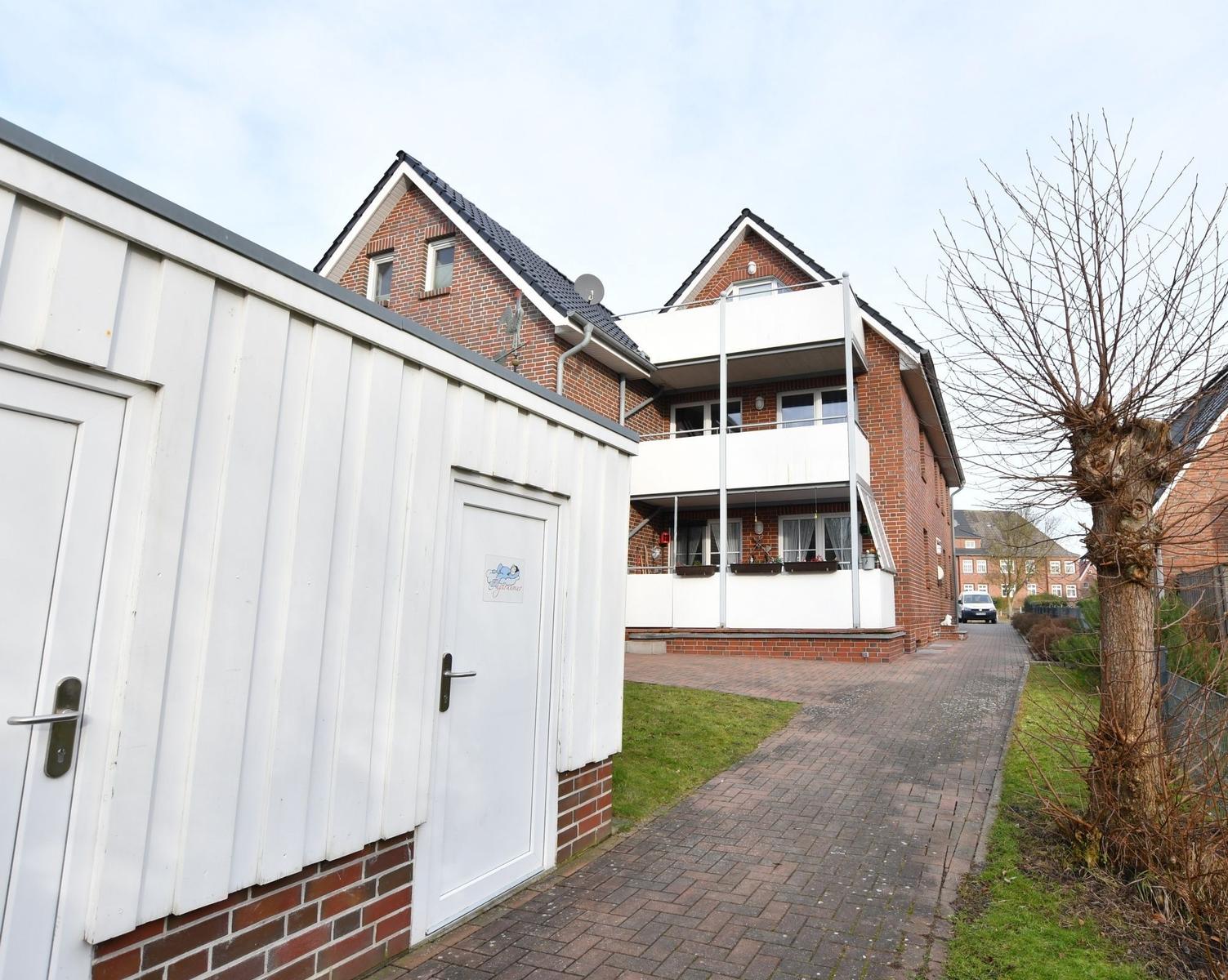 Haus mit Balkon, weiße Garage und gepflasterter Weg.