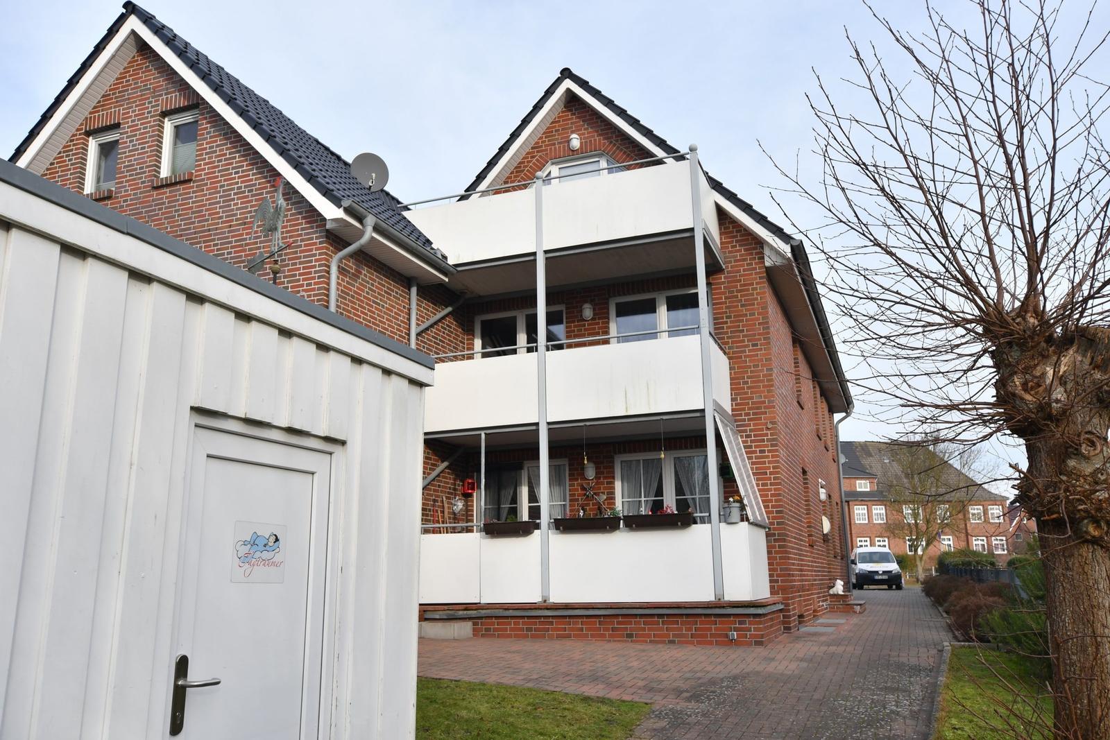 Zweistöckiges Haus mit Balkon und rotem Ziegelmauerwerk. Vor dem Haus steht ein weißer Container.