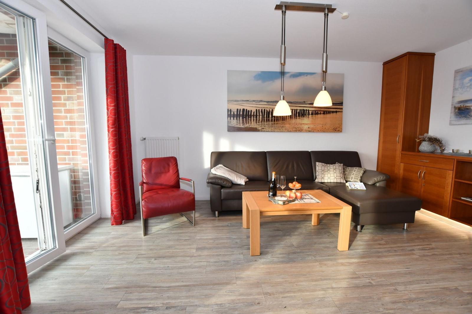 Wohnzimmer mit braunem Sofa, rotem Sessel und Holztisch. Große Glastür führt auf Balkon.