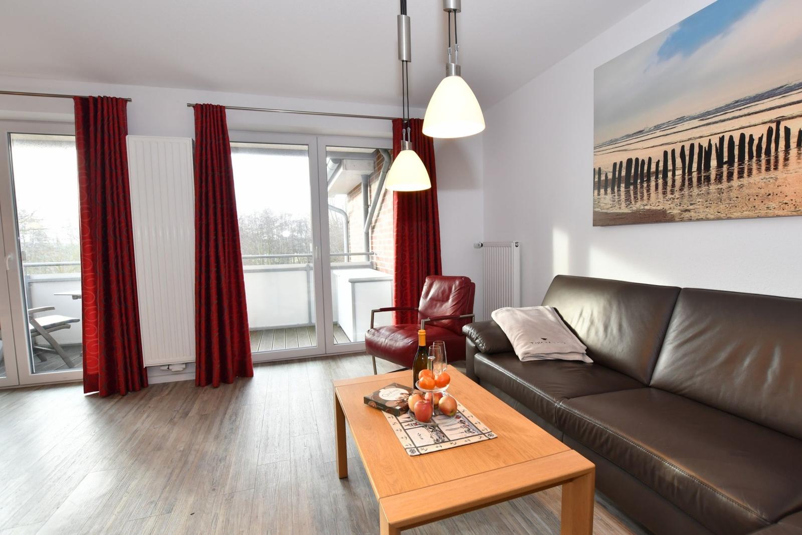 Wohnzimmer mit Sofa, Couchtisch und Balkon. Rote Vorhänge und Wandbild.