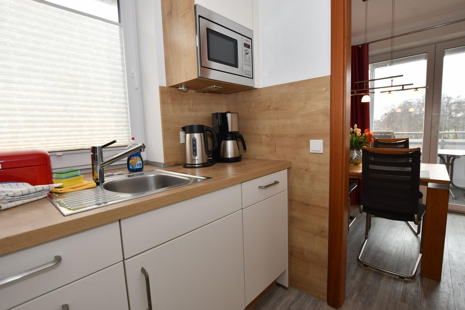 Küche mit Spüle, Mikrowelle und Kaffeemaschine. Durchgang zu Essbereich mit Tisch und Stühlen.