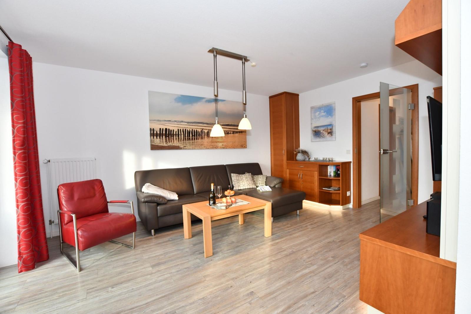 Wohnzimmer mit braunem Sofa, rotem Sessel und Holztisch. An der Wand hängt ein Bild.