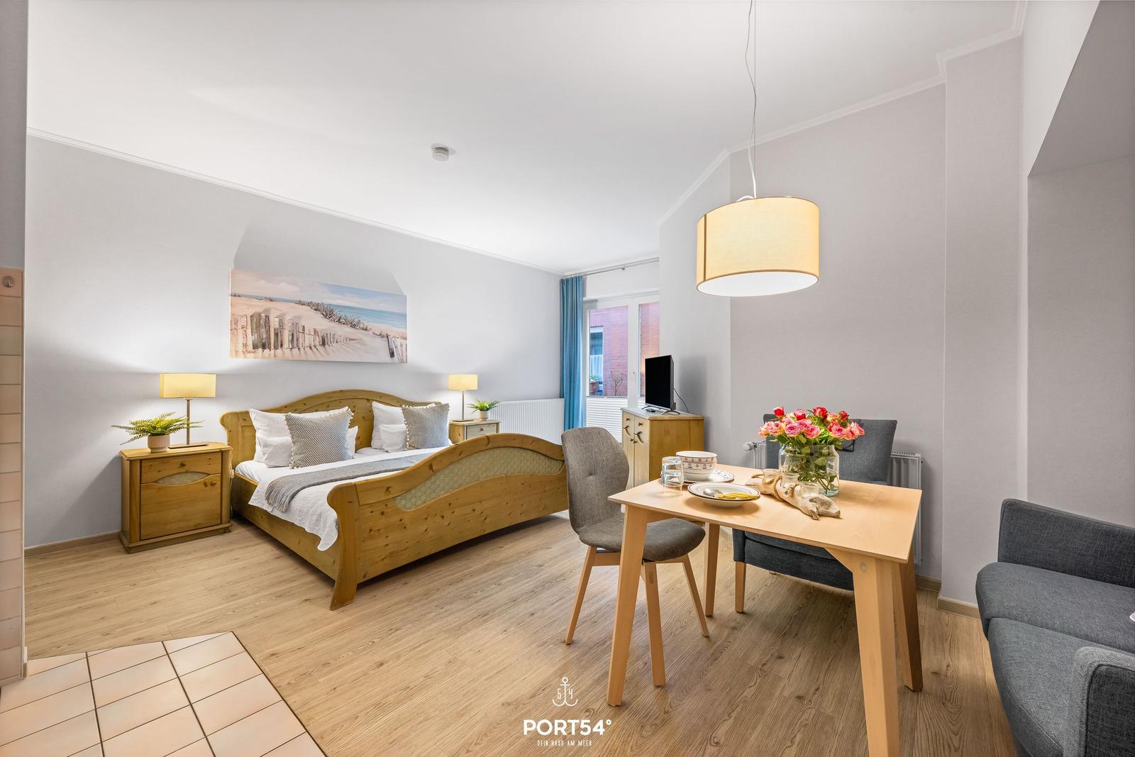 Schlafzimmer mit Bett, Tisch und Sofa. An der Wand hängt ein Bild.