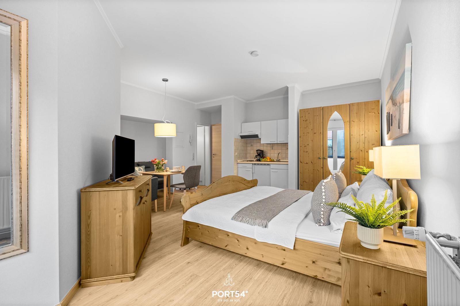 Schlafzimmer mit Holzbett, TV-Schrank und Blick in Küche und Essbereich.