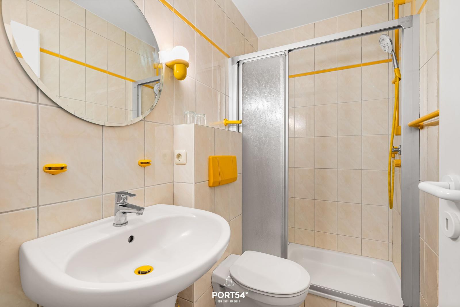 Badezimmer mit Dusche, Waschbecken und Toilette. Gelbe Akzente an den Wänden.