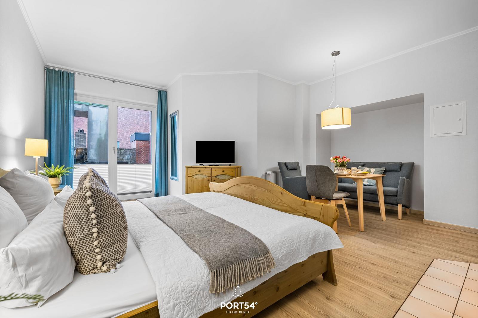 Schlafzimmer mit Bett, TV und Blick auf Balkon. Wohnbereich mit Sofa und Esstisch.