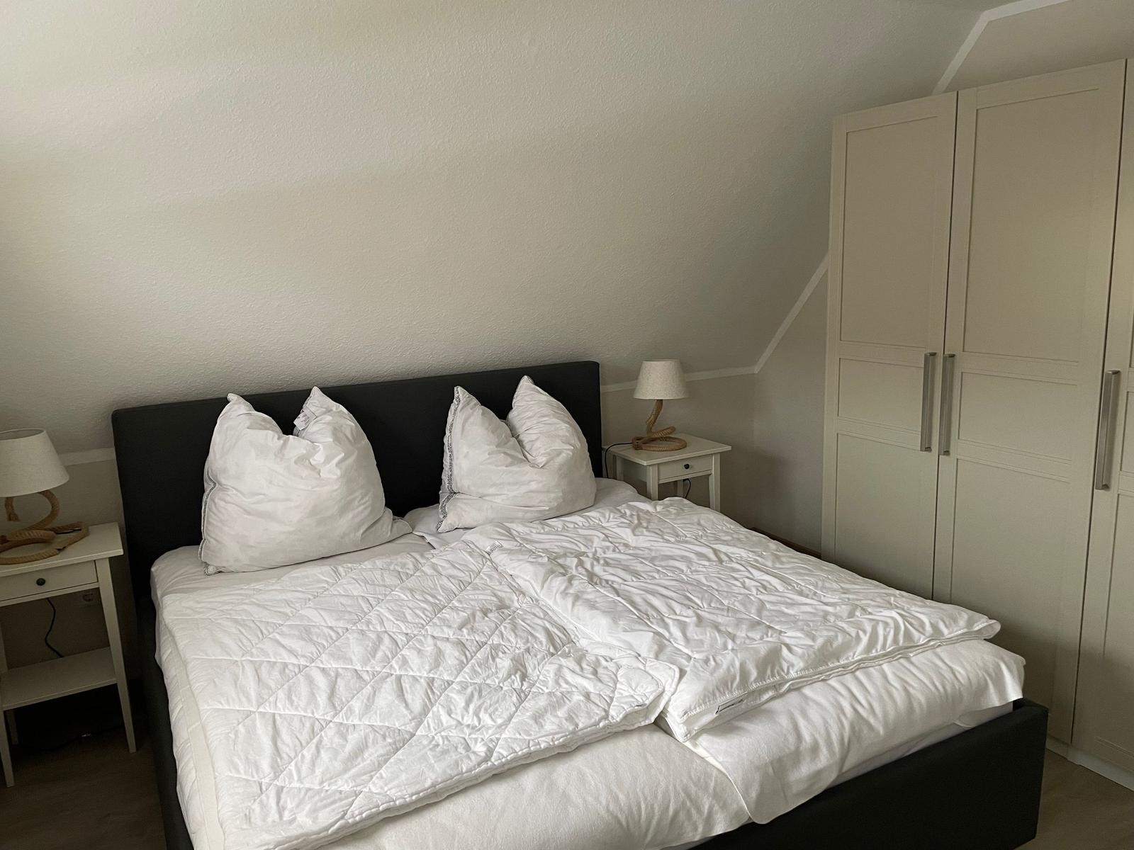 Schlafzimmer mit Doppelbett, weißen Nachttischen und Kleiderschrank.