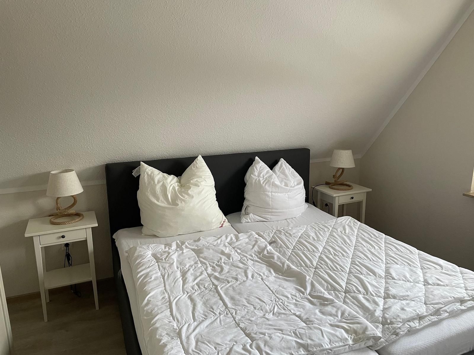 Schlafzimmer mit Doppelbett, zwei Nachttischen und Decke. Dachschräge im Hintergrund.