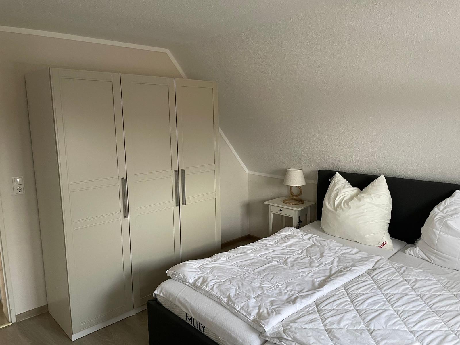 Schlafzimmer mit Doppelbett, Kleiderschrank und Nachttisch mit Lampe.