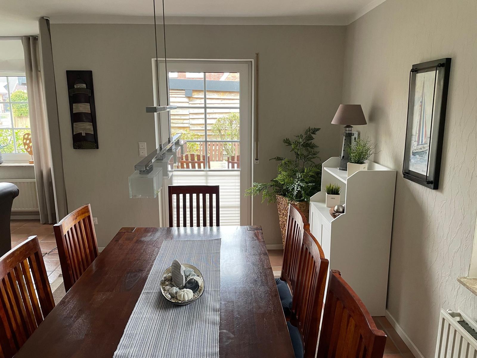 Esszimmer mit Holztisch, Stühlen und Blick auf Balkon.
