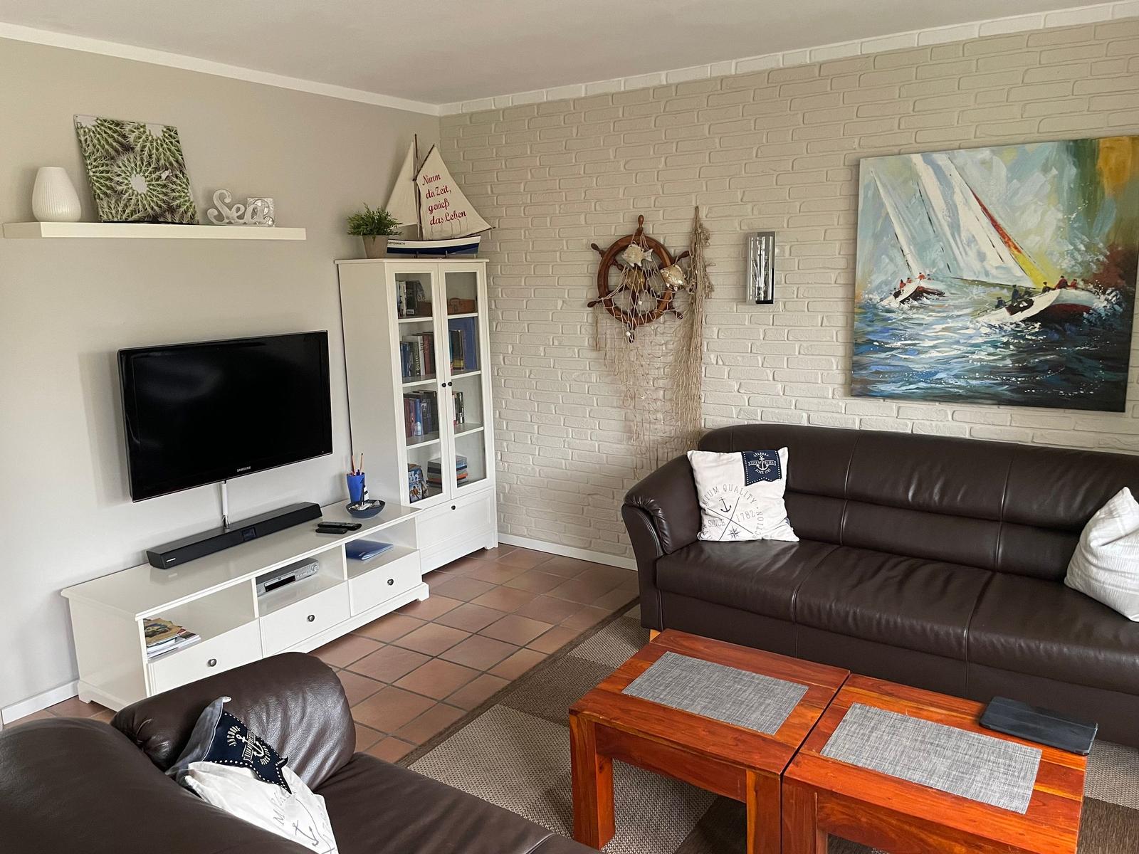 Wohnzimmer mit Sofa, Fernseher und Seemotiven an der Wand.
