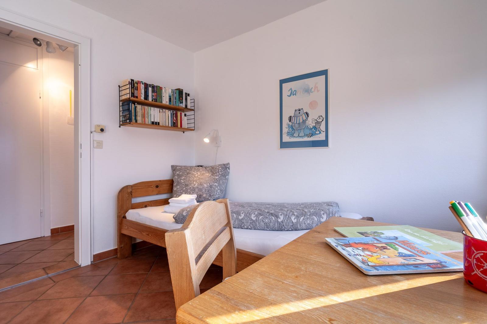 Ein Schlafzimmer mit Holzbett, Tisch und Bücherregal an der Wand.