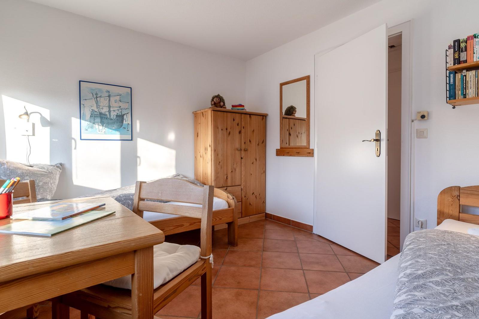 Zimmer mit zwei Betten, Holzmöbeln und Terrakottaboden. An der Wand hängt ein Bild eines Schiffs.