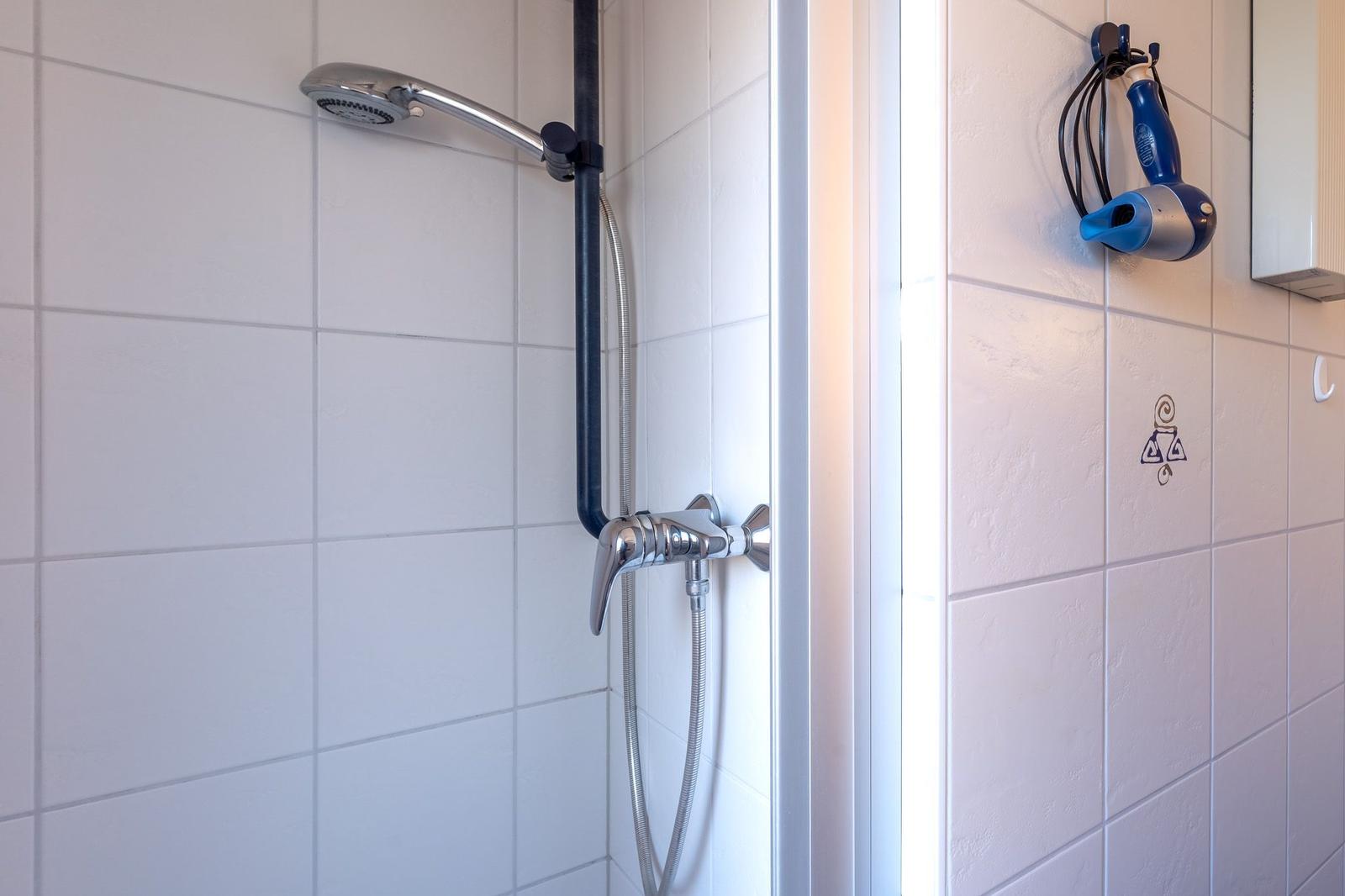 Dusche mit Handbrause und blauem Haartrockner an der Wand.