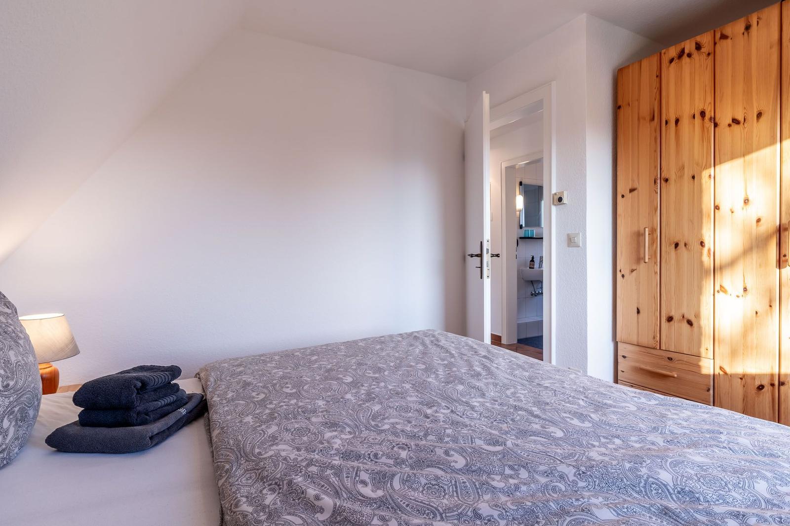 Schlafzimmer mit Bett, Holzschrank und Blick in das Badezimmer.