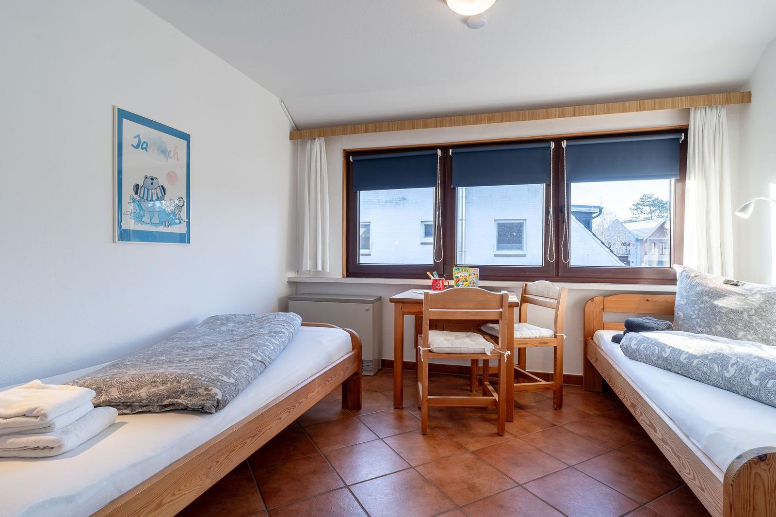 Zimmer mit zwei Betten, Tisch, Stühlen und Fenster mit Blick auf Gebäude.