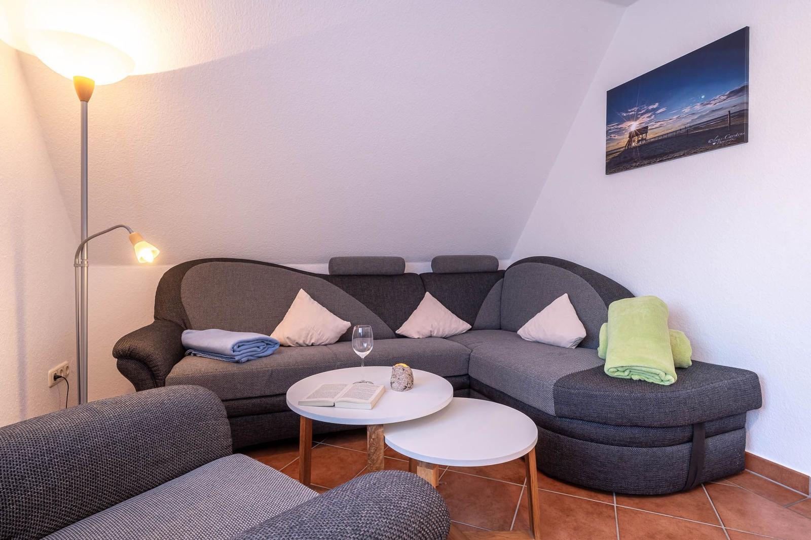 Ein Wohnbereich mit einem grauen Sofa, zwei runden Tischen und einer Stehlampe.