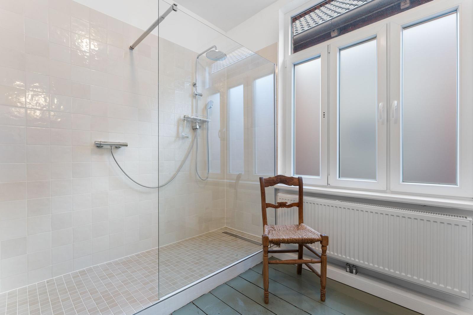 Dusche mit Glaswand, Holzstuhl und Fenster mit Milchglas