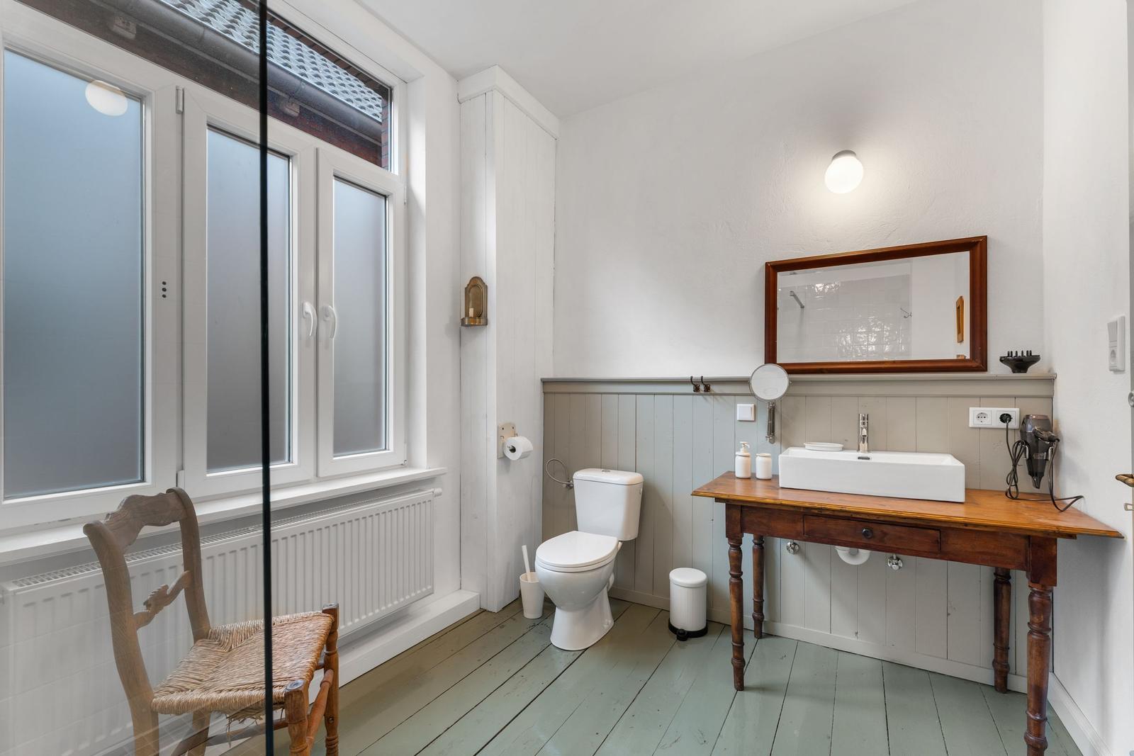 Badezimmer mit Toilette, Waschtisch und Fenster. Holzfußboden und rustikale Möbel.