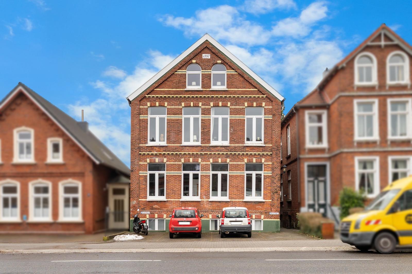 Rotes Backsteingebäude mit weißen Fenstern und Parkplätzen vorne.