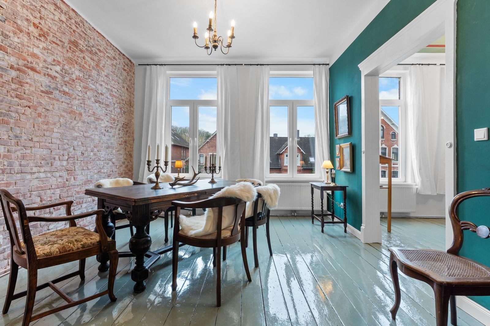 Esszimmer mit Holztisch, Stühlen und Steinwand. Fenster mit Blick auf Dächer.