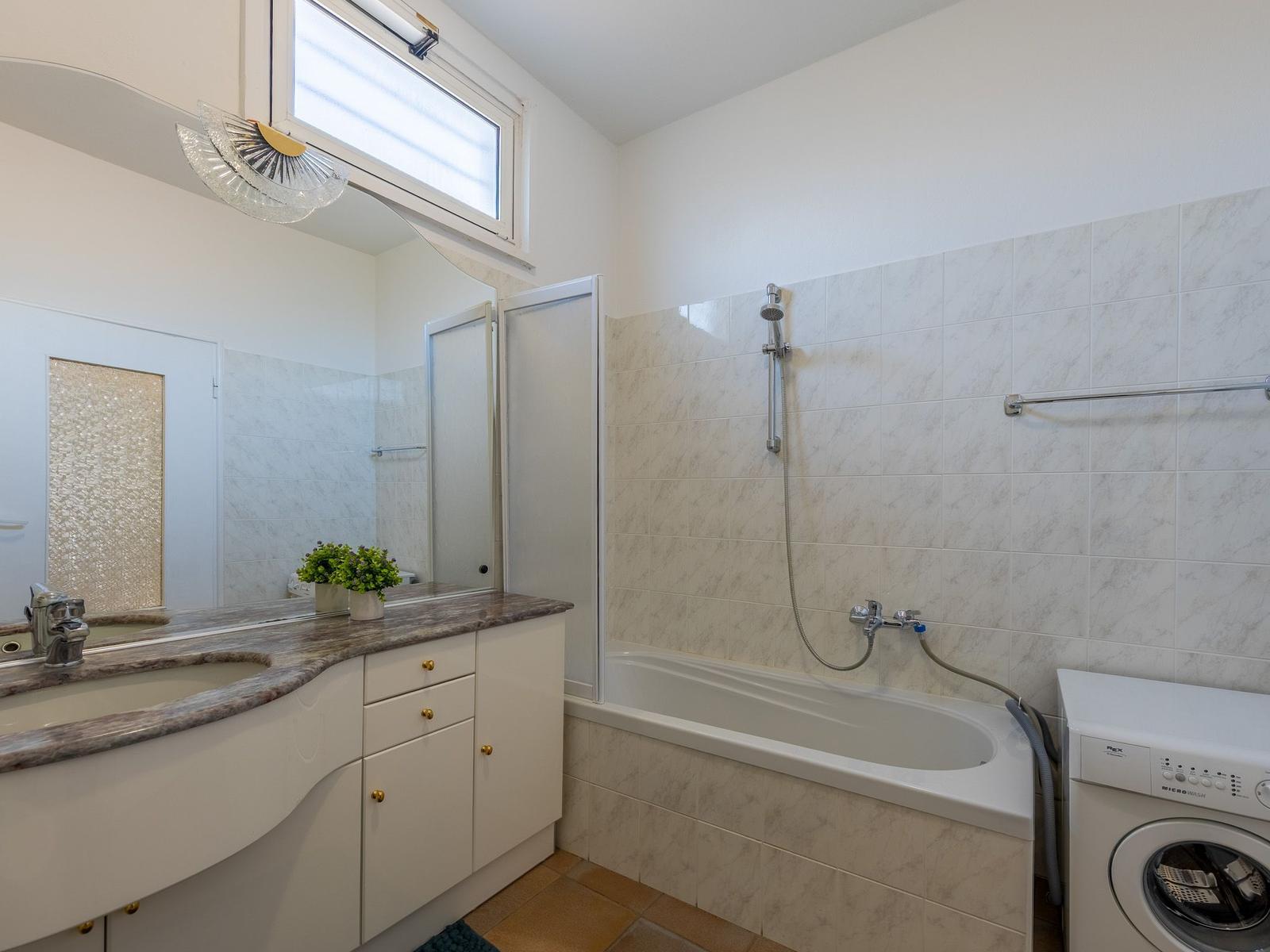 Badezimmer mit Badewanne, Dusche, Waschmaschine und Spiegelschrank.