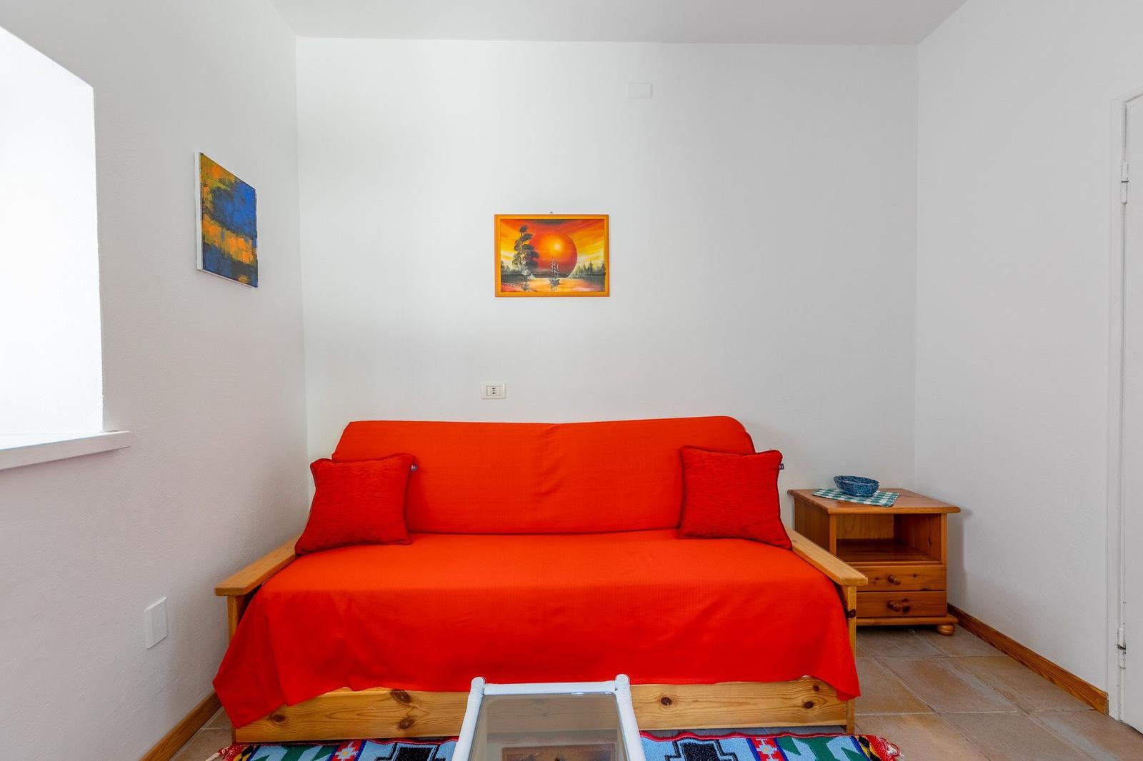 Ein Raum mit einem roten Sofa, zwei Kissen, einem Holztisch und zwei Wandbildern.