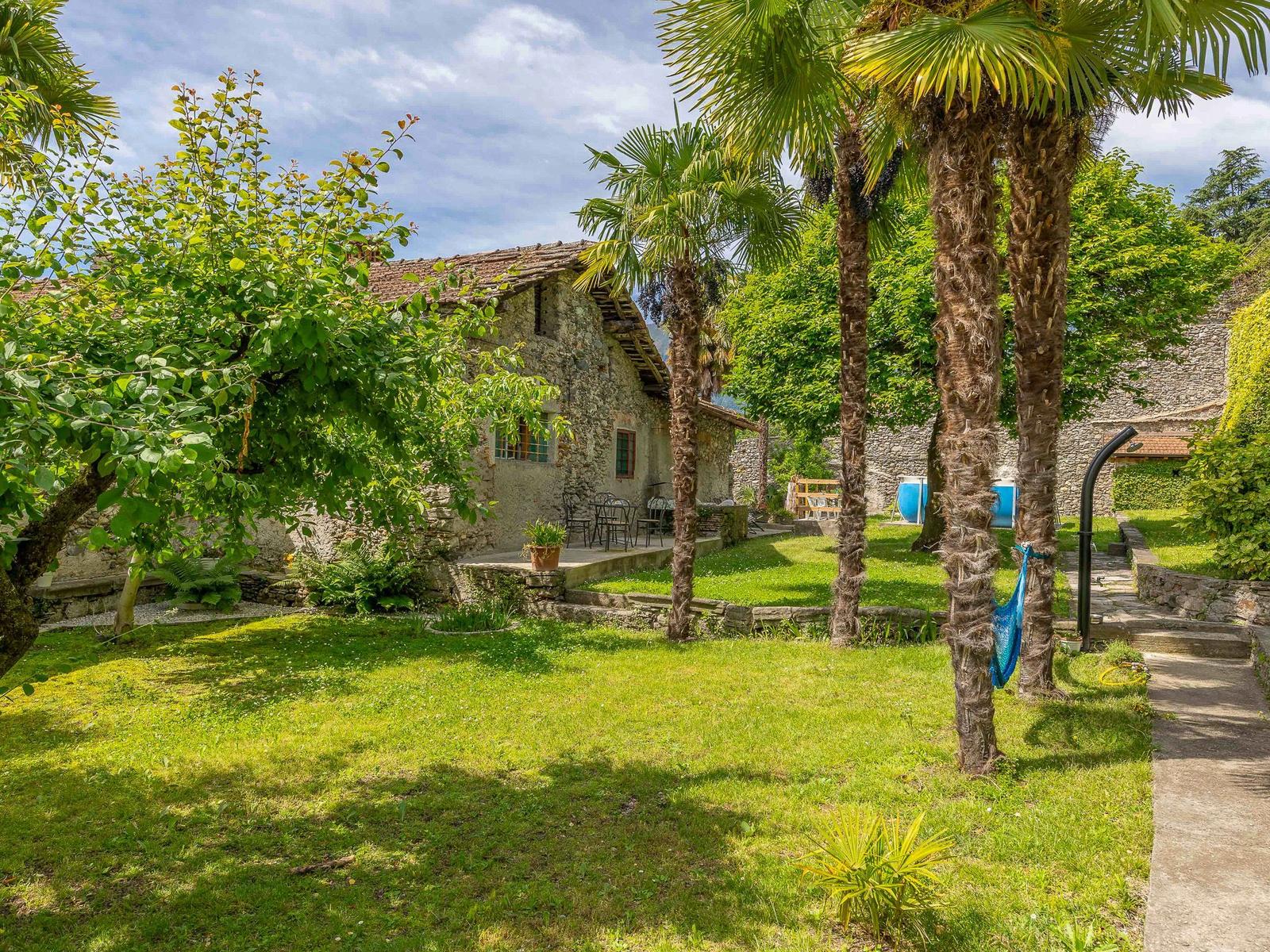 Steinhaus mit Garten, Palmen und Terrasse unter blauem Himmel.