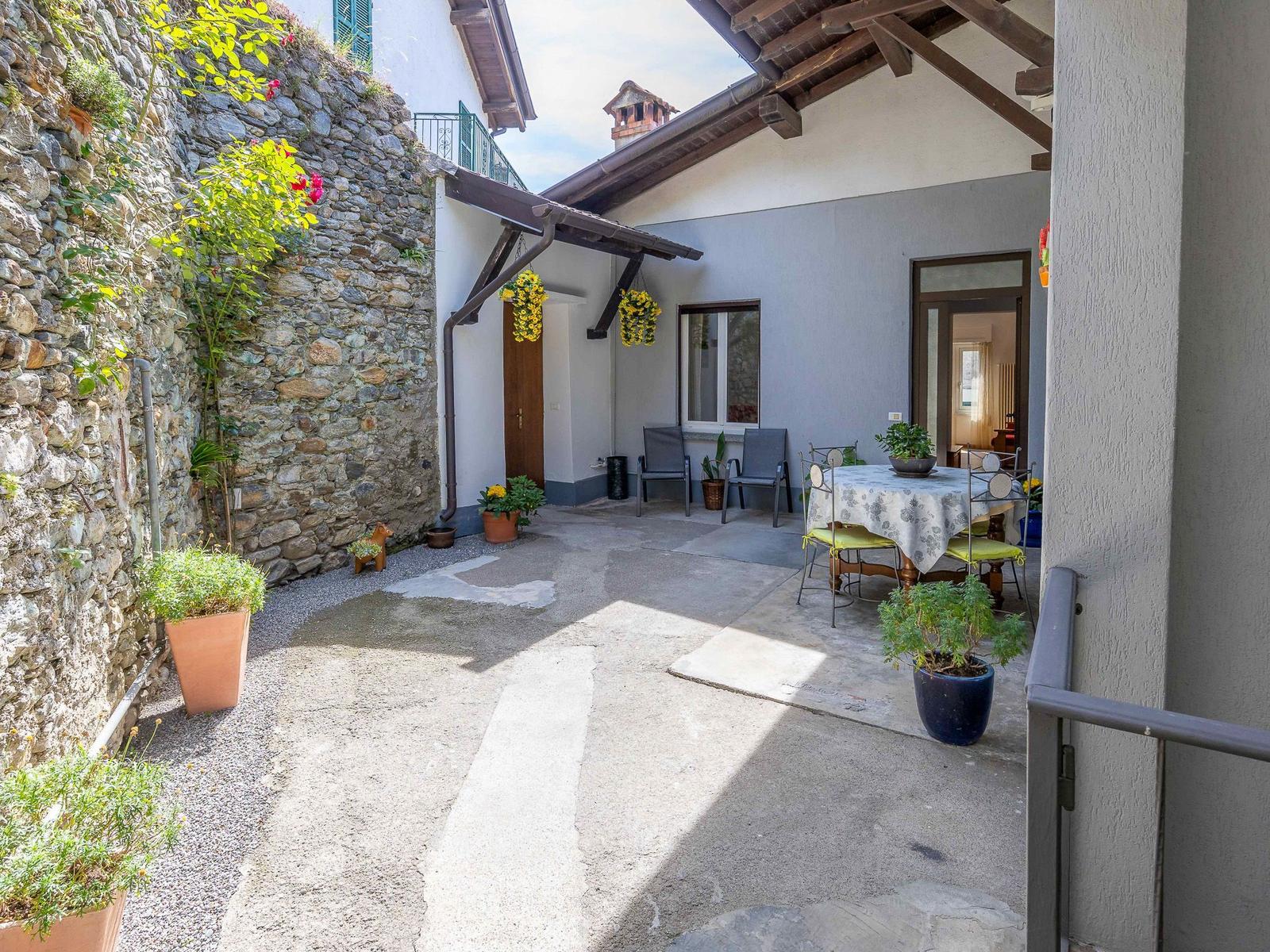 Terrasse mit Tisch, Stühlen und Pflanzen an Steinmauer und Hauswand.